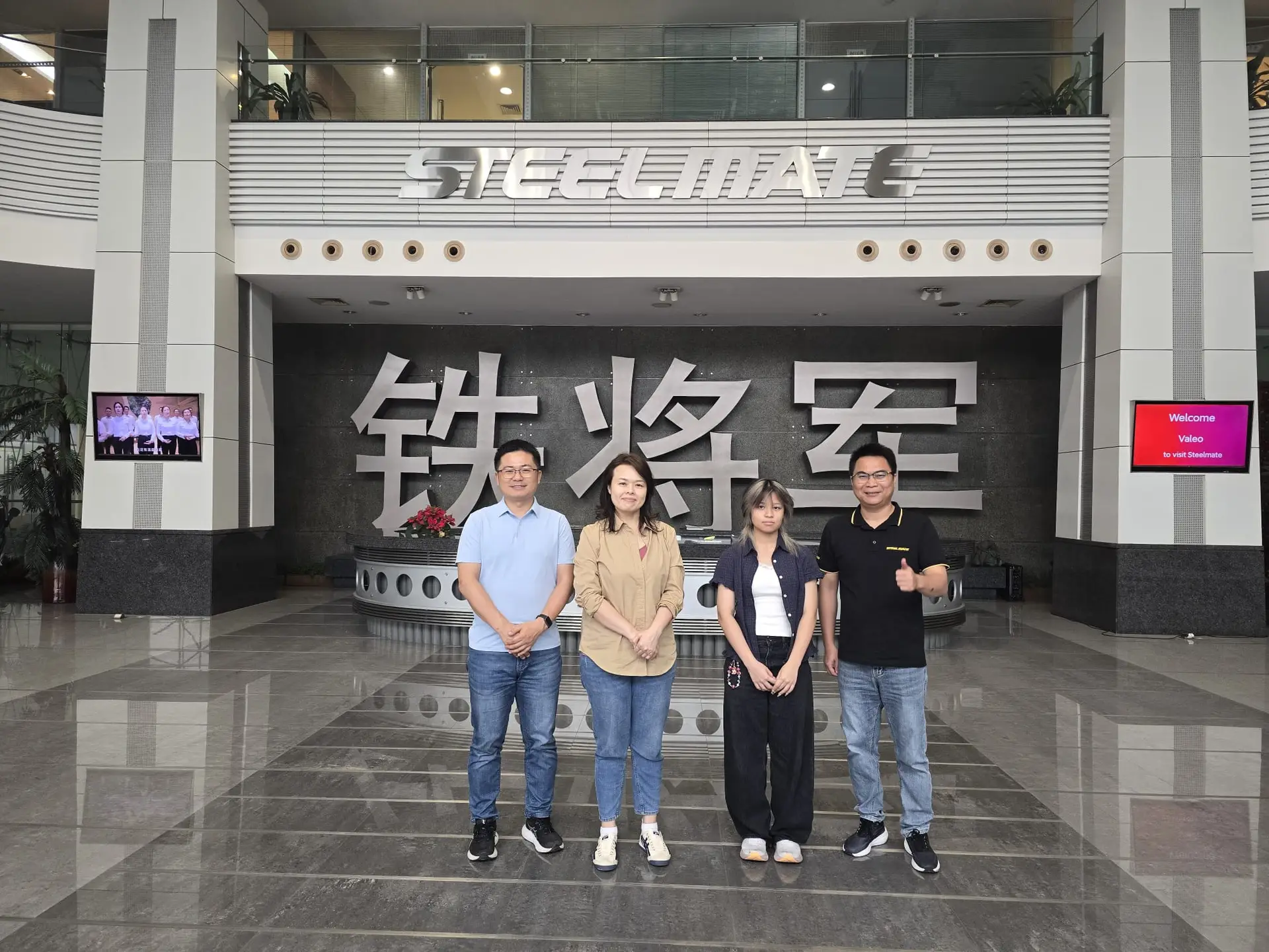 Five people stand in a modern lobby beneath a large steelmate sign and chinese characters on a dark wall behind them | tire pte ltd | tire pte ltd