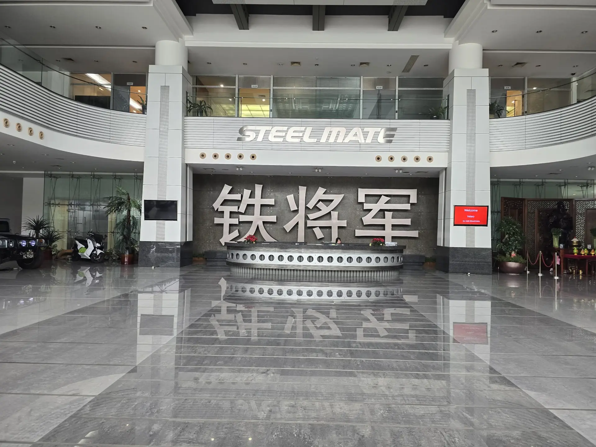Spacious modern showroom lobby with a curved railing steel sign reading steelmate and a large chinese character backdrop behind a circular reception desk | tire pte ltd | tire pte ltd